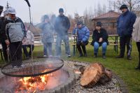Mieszkańcy ogrzewają się przy ognisku podczas spotkania w ogrodzie.